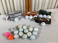 Golf balls both new in boxes and used scattered on white surface against a white slat wall background