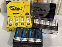 Full lot overview showing all boxes of Titleist NXT (yellow), Titleist Pro V1x (black/white), and Precept Ultra Distance (black/blue) golf balls in original packaging.