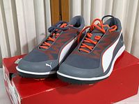 Pair of Puma walking and running shoes on top of red Puma box. Shoes are grey with orange accents and white Puma stripe along the side.