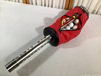 Full view of shag bag golf ball retriever showing the red fabric bag partially unzipped revealing various golf balls inside.