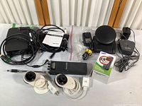Assortment of electronic devices including webcams, CB radio, Tele-zapper, cables, and a boxed Samsung mobile phone placed on a table.