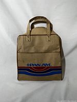 Front view of the tan canvas tote bag featuring Pan Am logo with red and blue stripes