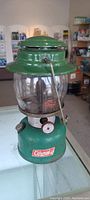 Full view of vintage green Coleman lantern with glass globe, metal base and valve control.