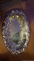 Top view of the antique silver oval tray showing embossed floral and scroll patterns on the raised rim and scratched central surface.