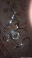 Photo showing four silver plated antique items on a patterned carpet, including a curved handle, a bulbous base piece, a round knob, and a small cross ornament.