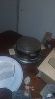 Waffle iron closed and seen from the side, showing metal body and wooden handles.