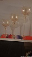 Three tall decorative glasses placed in a row showing size difference and clear view of etched design.