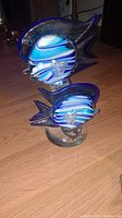 Pair of blue and clear glass fish figurines on wooden surface