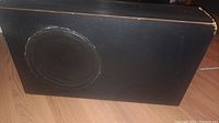 Front view of black speaker cabinet, showing circular speaker grille and some wear.