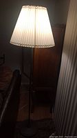 Floor lamp lit, showing white pleated fabric shade and black metal base in a room.