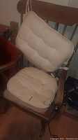 Front view of antique wooden rocking chair with beige tufted cushions tied on seat and backrest