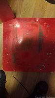 Red metal sign showing wear, holes, and faded spots on top side.