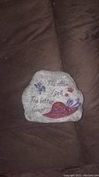 Photo showing the painted rock with inscription and floral decorations against a dark fabric background.