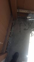 Three metal plant holders placed on concrete floor against wooden fence, showing wrought iron finish and decorative scroll legs.