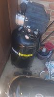 Full front view of the Central Pneumatic air compressor showing tank and partial motor assembly, outdoors near a brick wall.