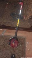 Photo of full weedwacker showing the shaft, handle, and shoulder strap.