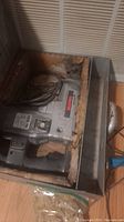 Rotary hammer power tool with visible control switches and power cord inside the metal case