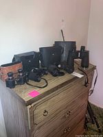 Five pairs of binoculars with cases arranged on wooden dresser, including various black and brown cases.