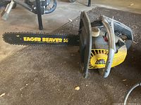 Full side view of yellow and black McCulloch Eager Beaver 14 chainsaw placed on floor showing entire length including handle and blade