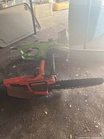 Two electric chainsaws on floor, one green Portland 24 with guard, one orange Remington without guard