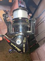 Close-up of Shakespeare BWS 700 black fishing reel with white fishing line spooled, showing brand and model details