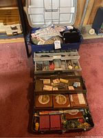 Two large tackle boxes open showing assorted fishing hooks, weights, floats, spools of fishing line, and other accessories organized in compartments and trays.