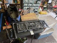 Photo showing hand tools including wrenches, pliers, hammers, screwdrivers, miter boxes, saw in carrying bag, and coolers on a table.
