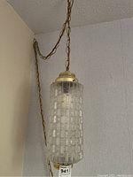 Close-up of glass hanging swag lamp with textured cylindrical shade and brass fittings, showing chain suspension.