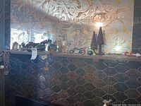 Photo showing the mantel with various decorative items including small framed pictures, model motorcycles, wooden Christmas trees, and other carved wooden items arranged along its length.
