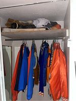 Closet view with hanging jackets and top shelf of hats and footwear