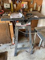 Photo showing full front view of Craftsman table saw on metal stand in a workshop setting with accessories and instruction manual on top.
