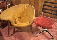 Mustard fabric armchair next to red vinyl rolling chair in basement setting