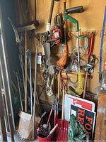 Full view of yard and garden tools against wall including chainsaw, trimmer, shovels and assorted hand tools