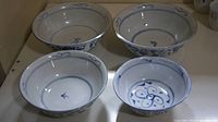 Four antique white porcelain bowls with blue painted designs inside and around the rim shown from above.