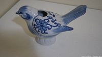 Side view of blue and white ceramic bird figurine showing floral painted patterns and open cavity on top.