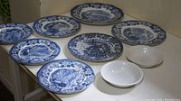 Nine pieces of blue and white transferware plates and two white bowls arranged on a table