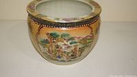 Side view of the fish bowl showing floral and traditional Chinese landscape paintings on a yellow background with a decorated rim.
