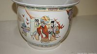 Close-up of the ceramic plant pot showing hand-painted traditional Asian figures and decor.