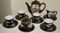 Full view of the tea set laid out, showing teapot, sugar bowl, creamer, six cups, and saucers with hand-painted traditional figures and gold details