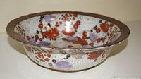 Side angle photo showing the bowl with red, purple, white flowers and brown embossed rim.