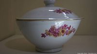 Side view of white porcelain lidded dish with floral pattern and gold trim.