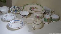 Photo showing 12 pieces of mixed bone china including cups, saucers, plates, small creamer, and sugar bowl with floral patterns and gold trim.