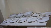 Full view of all 10 plates and bowls arranged in two rows showing floral decoration around edges.