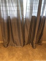 Close-up of gray silk drapes pooling slightly onto carpeted floor, showing material quality and color.
