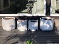 Four white round pots arranged on a deck in sunlight showing two larger and two smaller sizes with horizontal ribbed texture.