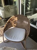 View of the wicker patio chair showing full front profile with cream cushion on base.