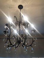 Full view of the Pottery Barn Celeste chandelier hanging from ceiling, showing six candle-style arms with attached glass crystals and metal chain mount.