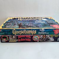 Side view of the two Goosebumps board games stacked, showing the titles Haunted Ruins and Terror in the Graveyard on the sides of the boxes.