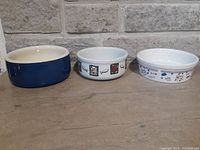 Three ceramic pet bowls shown side by side from the outside, displaying different colors and design motifs.