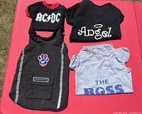 Four dog T-shirts including black AC/DC logo, black with Angel and halo, gray 'The Boss', and black winter coat with reflective stripes and paw patch